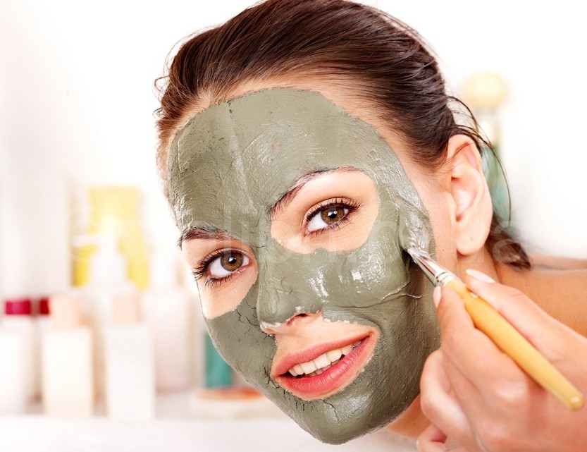 Woman with clay facial mask in beauty spa.